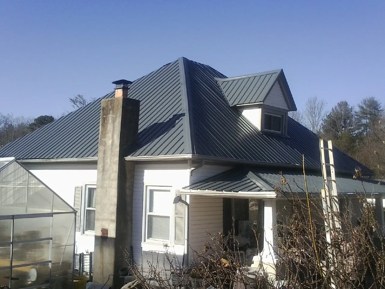 Dark blue standing seam metal roof on a white farmhouse with dormer — Slate & Tile Roof Repair by Roofing Brothers in Covington
