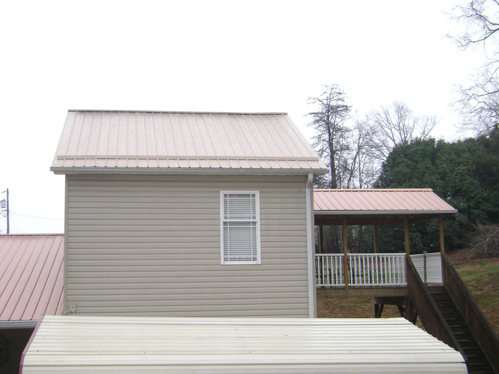 Tan metal roofs on a two story addition and attached porch, from a Roof Replacement job in Covington